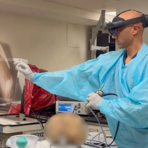 A person in medical scrubs and gloves is performing a procedure in a laboratory setting. They are using a handheld endoscopic instrument while interacting with a large monitor displaying an internal anatomical image.